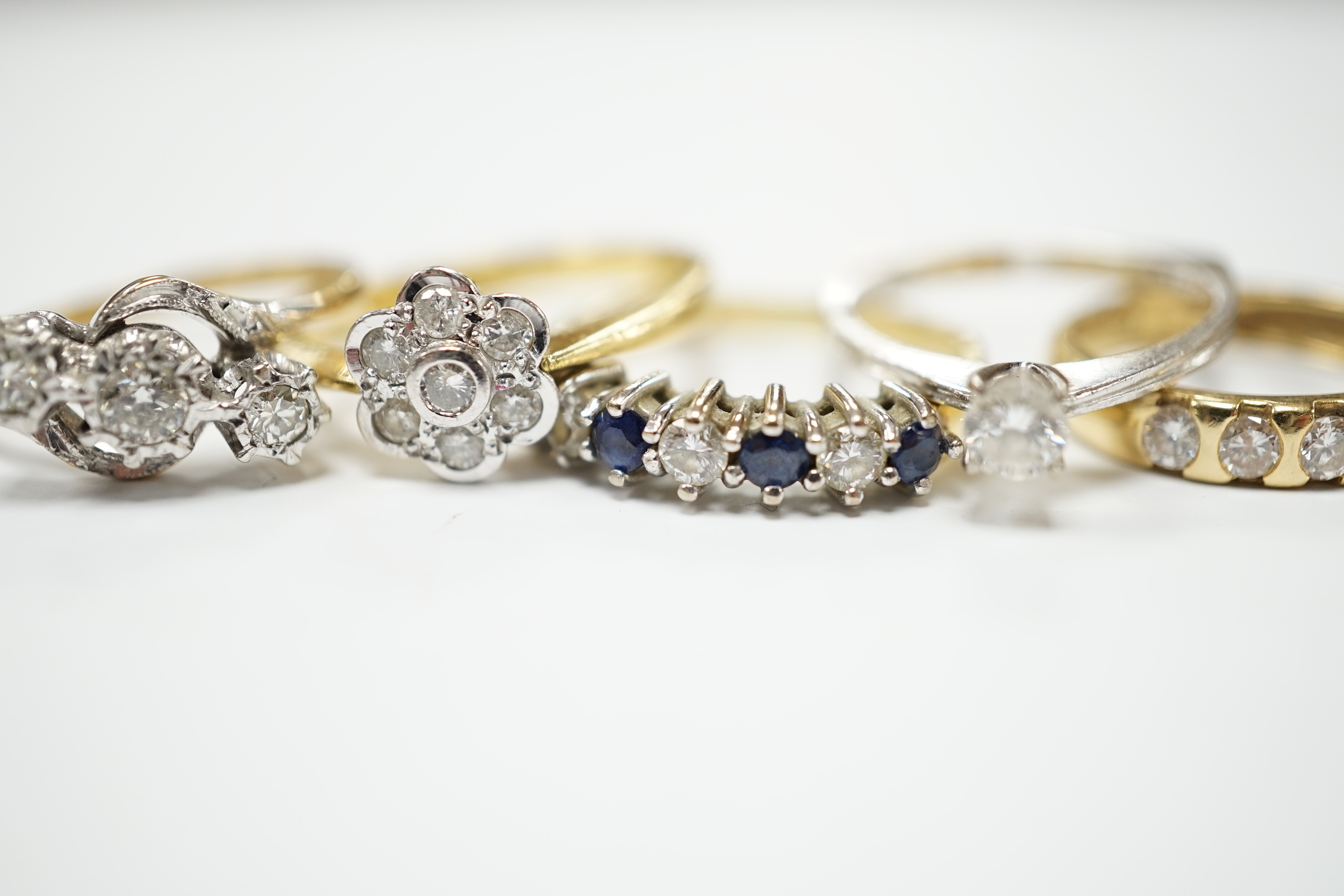 Four assorted 18ct and diamond set rings, including solitaire, flower head cluster, three stone crossover and seven stone half hoop, together with and 18ct sapphire and diamond set half hoop ring, gross weight 15.6 grams